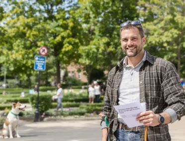 Un homme souriant dans la rue avec son chien au second plan